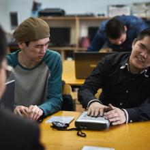 Two young men sitting at a library desk working with new Daisy players. The instruction booklet is on the desk.