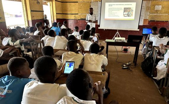A librarian teaches school students in a school classroom online safety skills, using a whiteboard and projector for slides.
