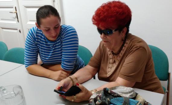 Senior using smart phone, with their trainer, in the library.