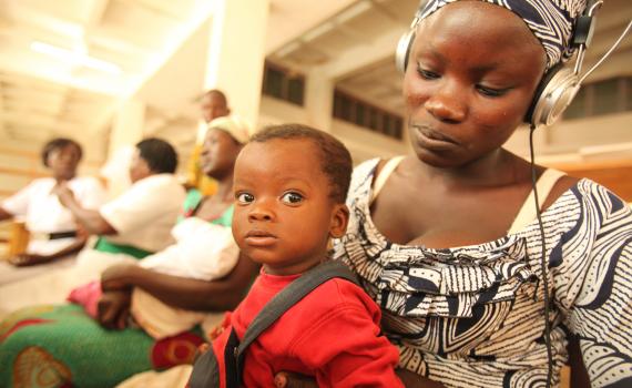 A young mother with her baby on her lap views health videos in the library's maternal health corner.